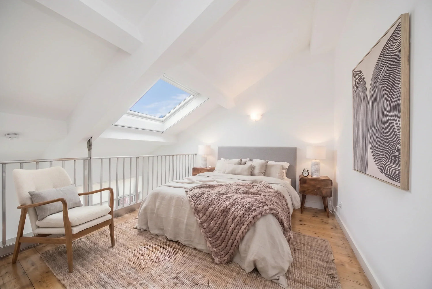 Mezzanine bedroom in an East End loft apartment with compact bedside tables, armchair and neutral styling.